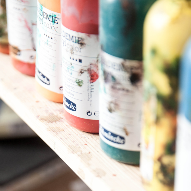 see-through bottles of colorful paints arranged across a wooden shelf.